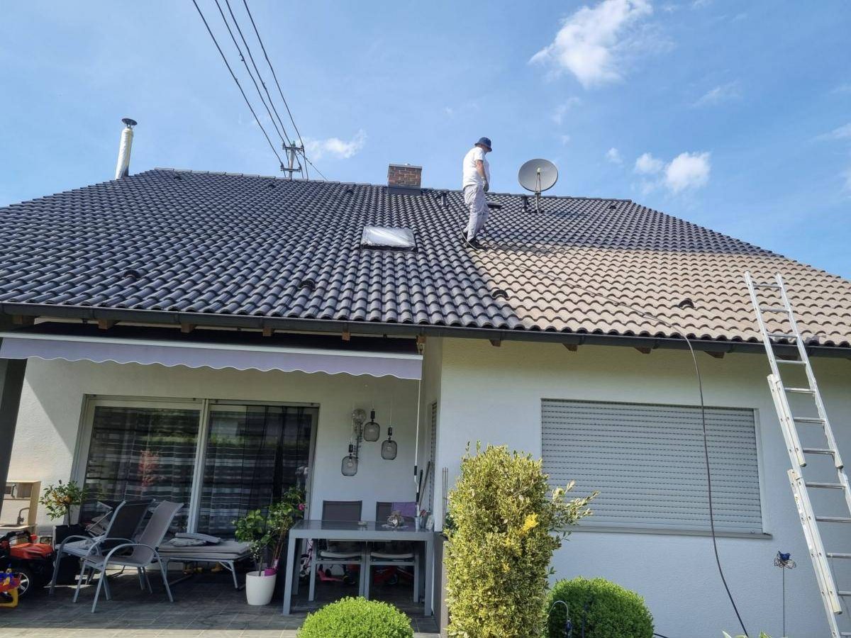 Mitarbeiter von Clean Stone beschichtet ein Ziegeldach: links bereits dunkel beschichtet, rechts noch alt